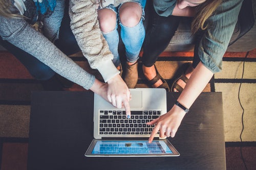 multiple people pointing at a macbook